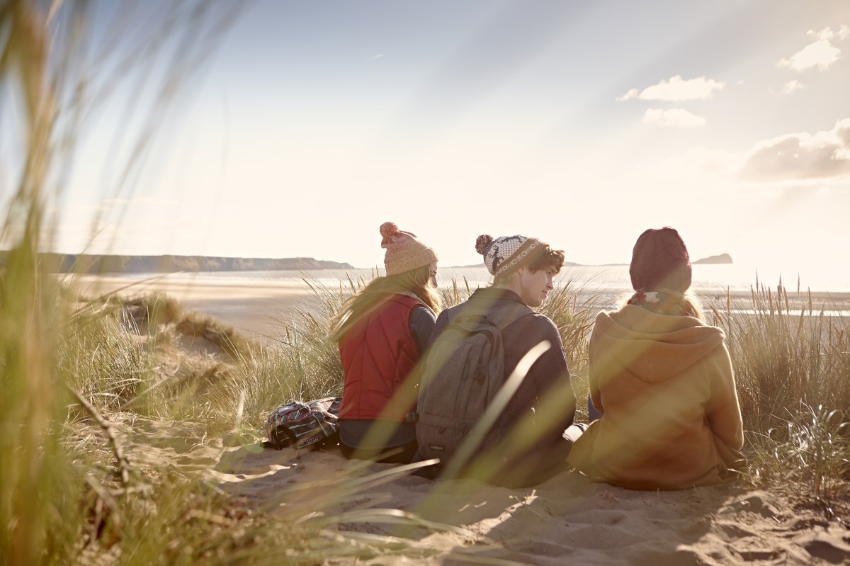 Three students sitting on a sand dune and looking across to the sea
