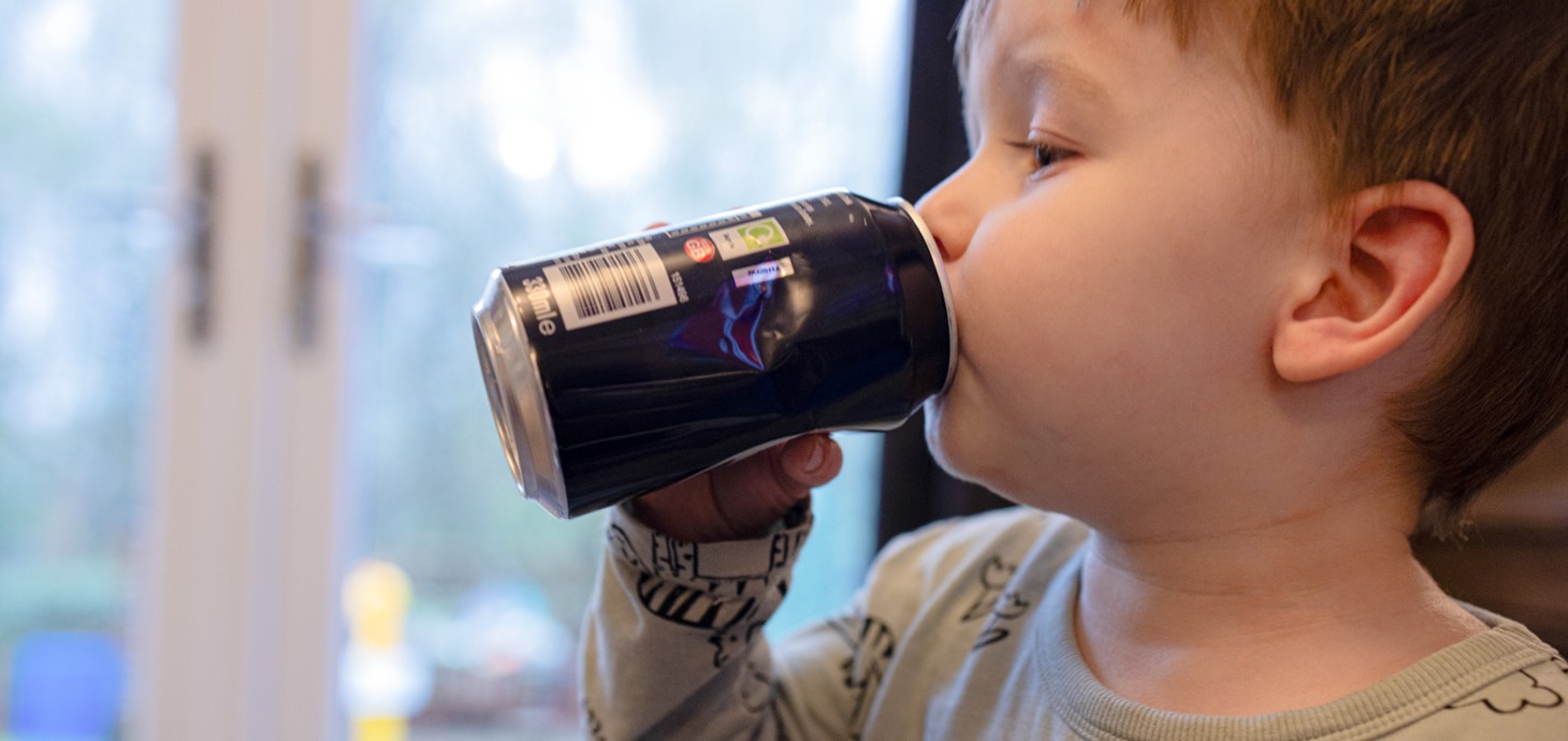 A young child drinking a fizzy, sugar-sweetened drink.