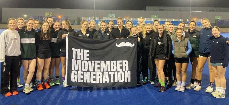 Hockey players holding a Movember flag on the hockey field after their triple header movember hockey fixture. 